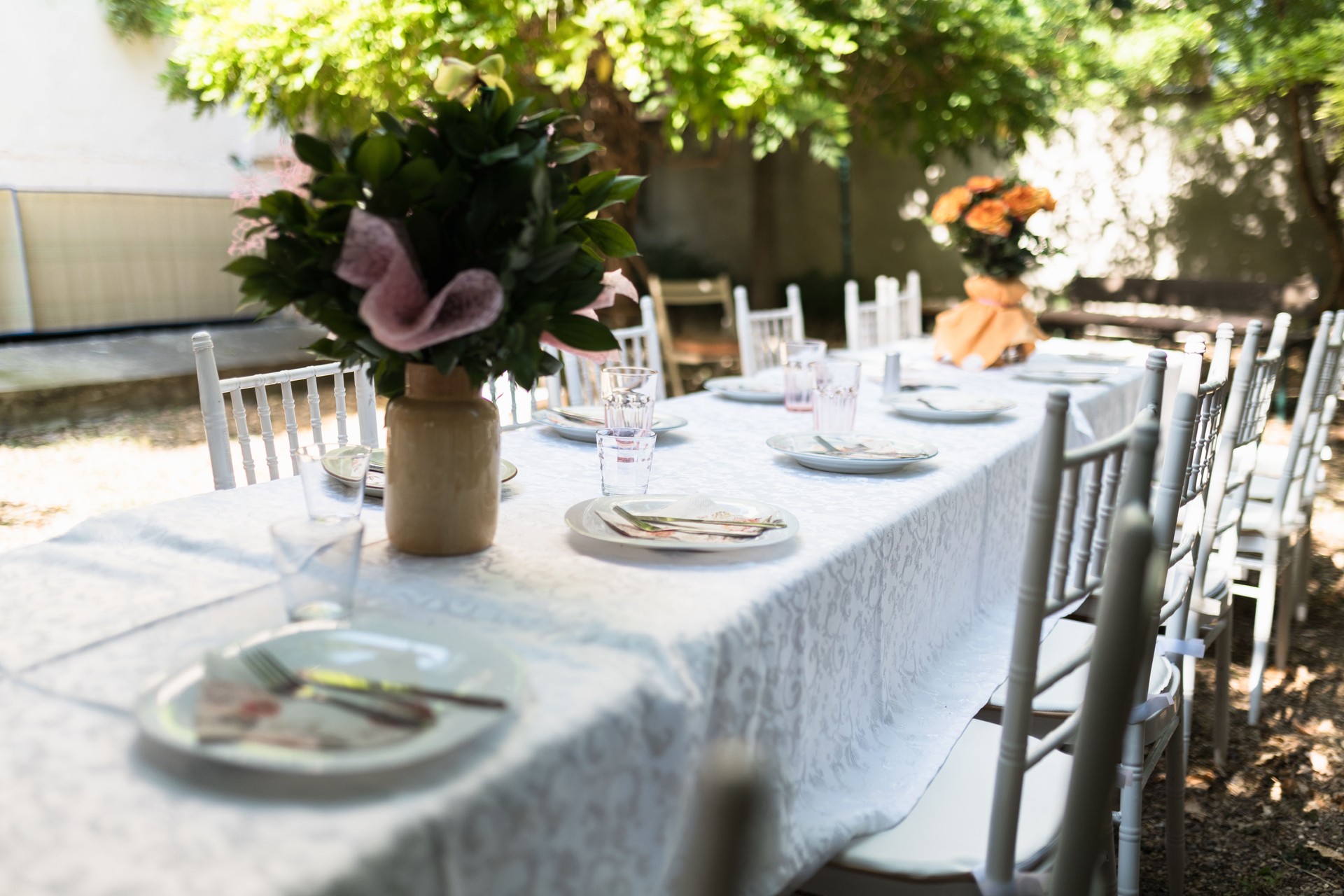 Elegant outdoor dining setup with floral centerpieces in a sunlit garden during late afternoon